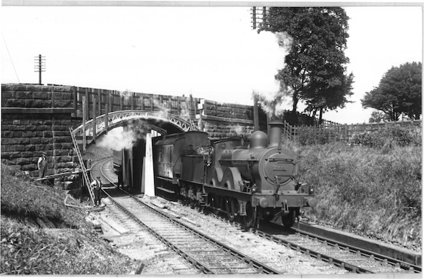 Photograph of workmen looking on as Midland Railway 1400 Class 2-4-0 No. 209 heads an express passenger train under a bridge that is supported by temporary timbers while it is being rebuilt.