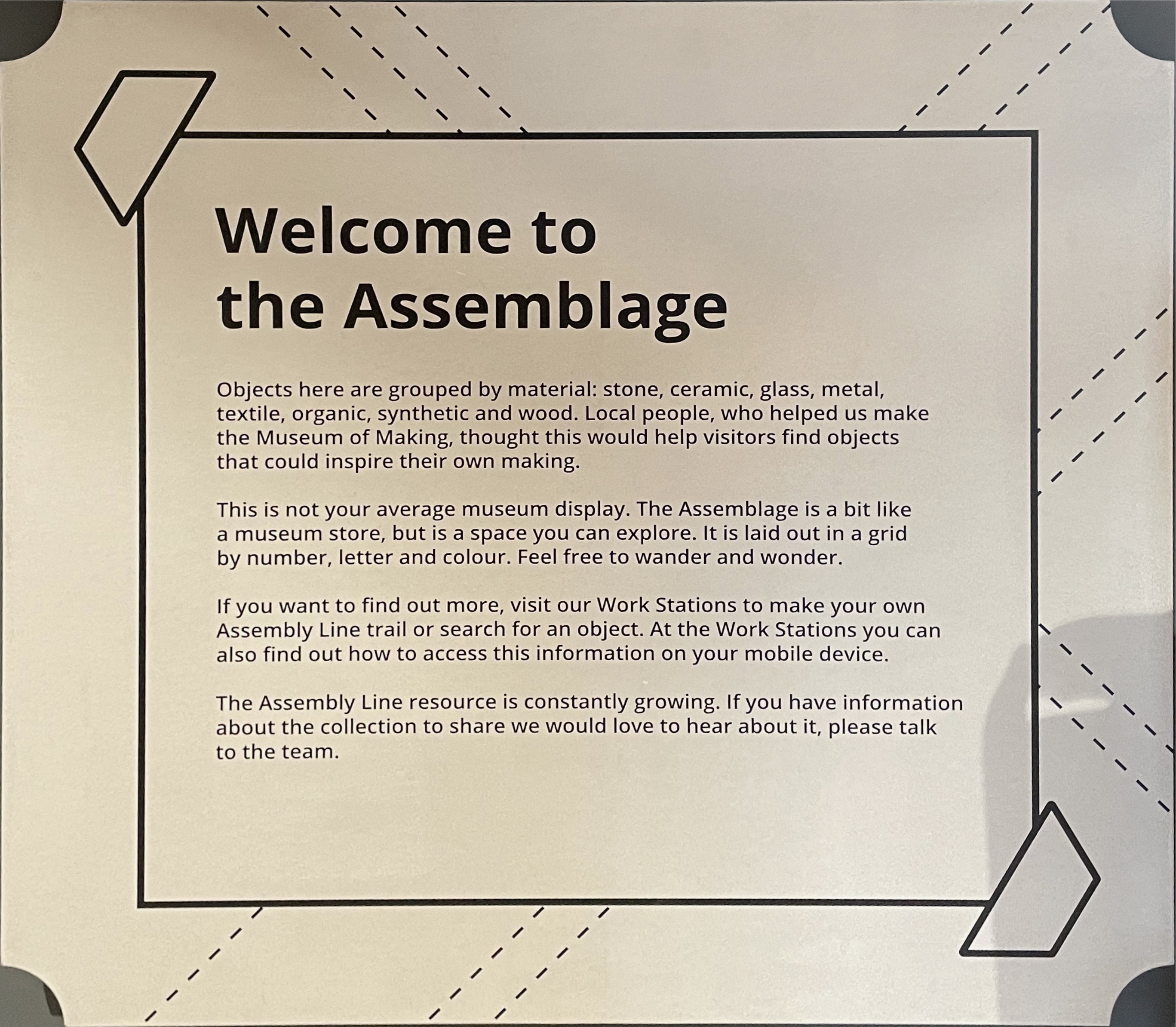 A sign that reads as follows; Welcome to
        the Assemblage Objects here are grouped by material: stone, ceramic, glass, metal, textile, organic, synthetic and wood. Local people, who helped us make the Museum of Making, thought this would help visitors find objects that could inspire their own making. This is not your average museum display. The Assemblage is a bit like a museum store, but is a space you can explore. It is laid out in a grid by number, letter and colour. Feel free to wander and wonder. If you want to find out more, visit our Work Stations to make your own Assembly Line trail or search for an object. At the Work Stations you can also find out how to access this information on your mobile device. The Assembly Line resource is constantly growing. If you have information about the collection to share we would love to hear about it, please talk to the team.