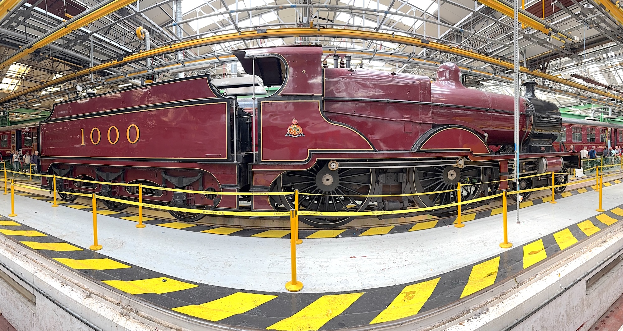 Midland Railway 4-4-0 Compound steam locomotive No.1000 on display insoide G Shop of the Litchurch Lane Carriage & Wagon Works for The Greatest Gathering on 3rd August 2025. A fish-eye lens effect prominates.