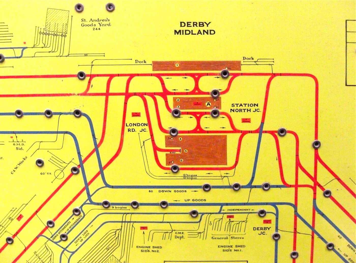 A pale green board with a diagrammatic representation of the railway lines and sidings around Derby station, each of which have holes in which pegs can be placed