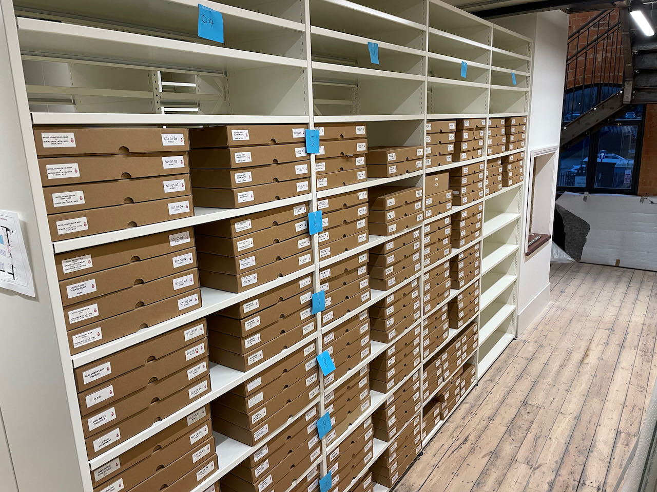 A row of cream coloured metal racking with dozens of tan boxes on them