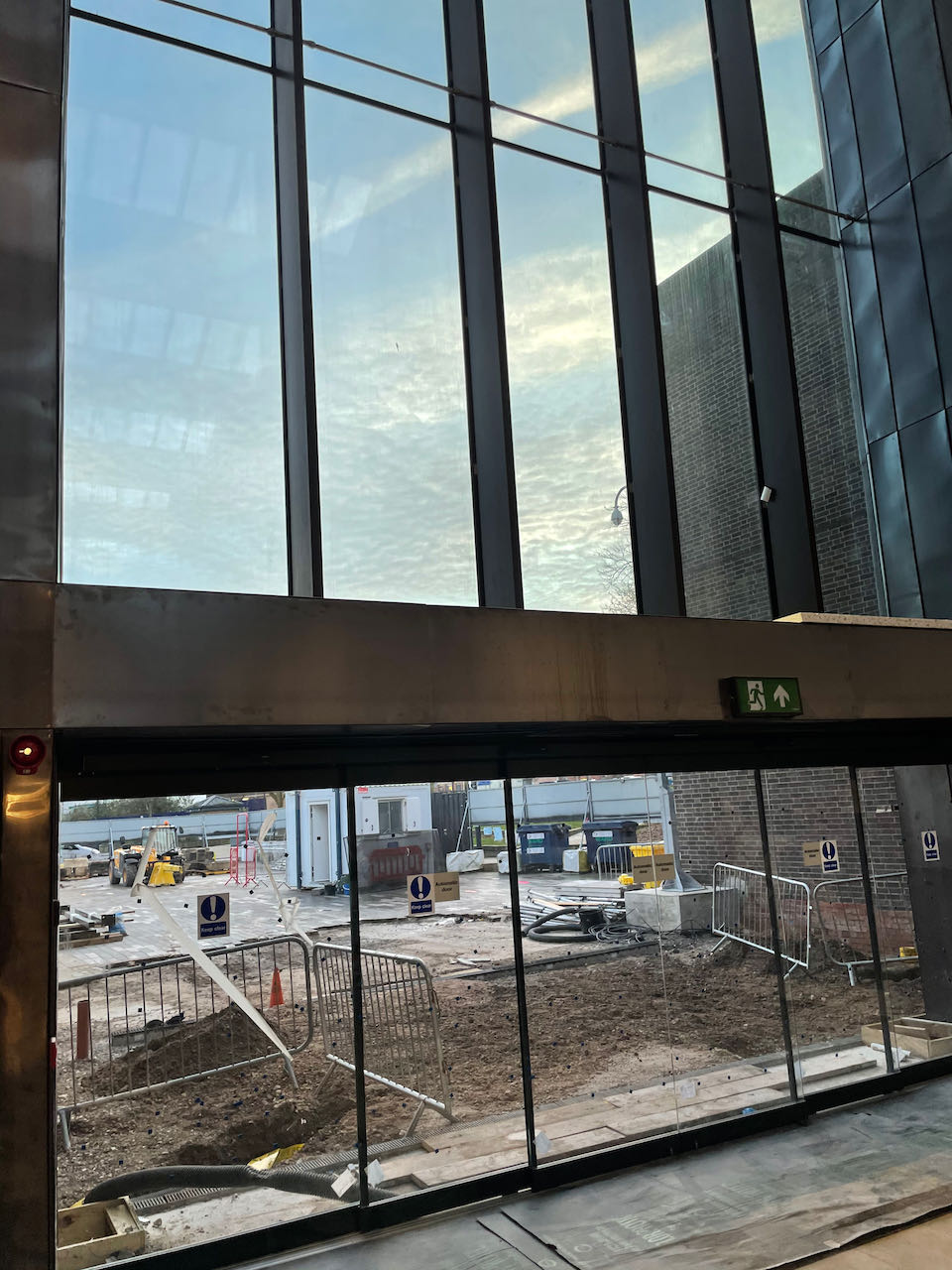 Looking outside through the wide glass front doors into what remains a building site outside