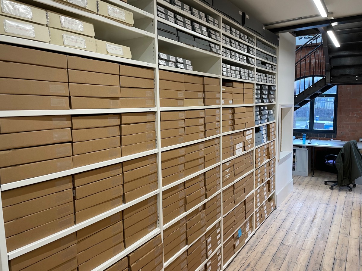 Rows of light coloured steel shelves filled with tan boxes