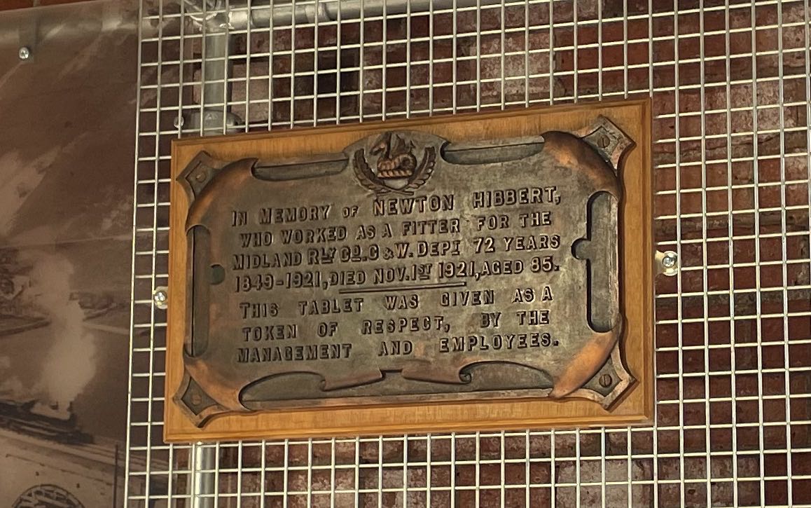 Bronze plaque which IN MEMORY OF NEWTON HIBBERT. WHO WORKED AS A FITTER FOR THE MIDLAND RLY CO. C&W. DEPT 72 YEARS 1849-1921, DIED NOV. 1ST 1921, AGED 85. THIS TABLET WAS CIVEN AS A TOKEN OF RESPECT, BY THE MANAGEMENT AND EMPLOYEES.