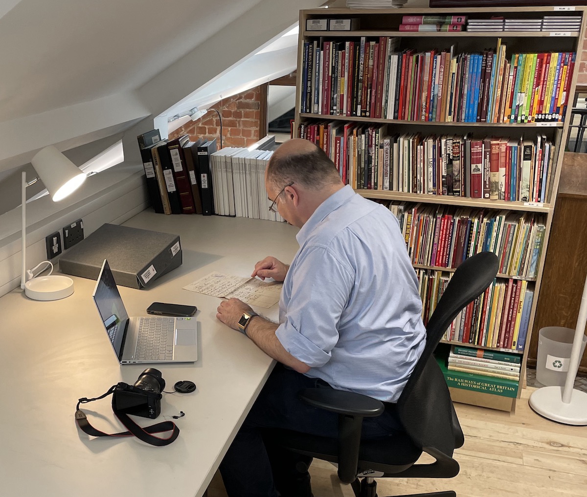 A man sitting at a desk in the Midland Railway Study Centre reading room and looking at a document