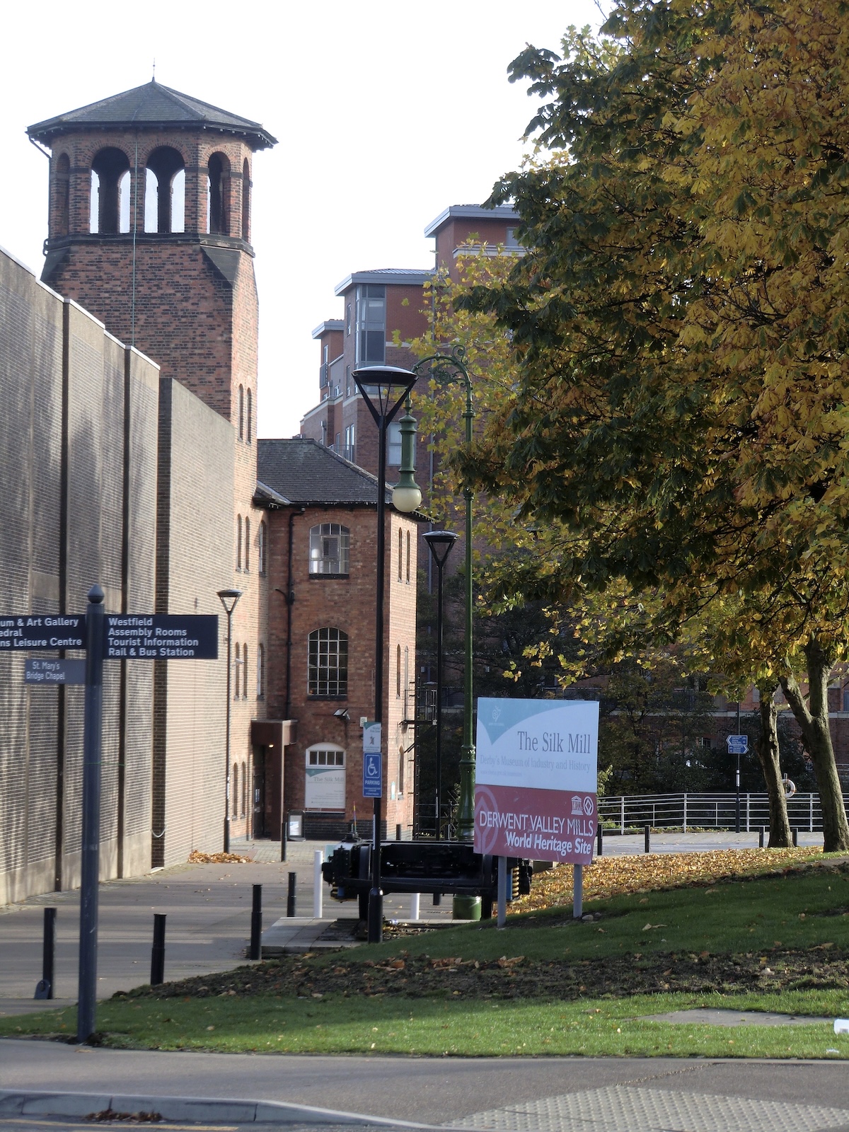 Red brick building with tower, trees, and signs in a park-like setting..