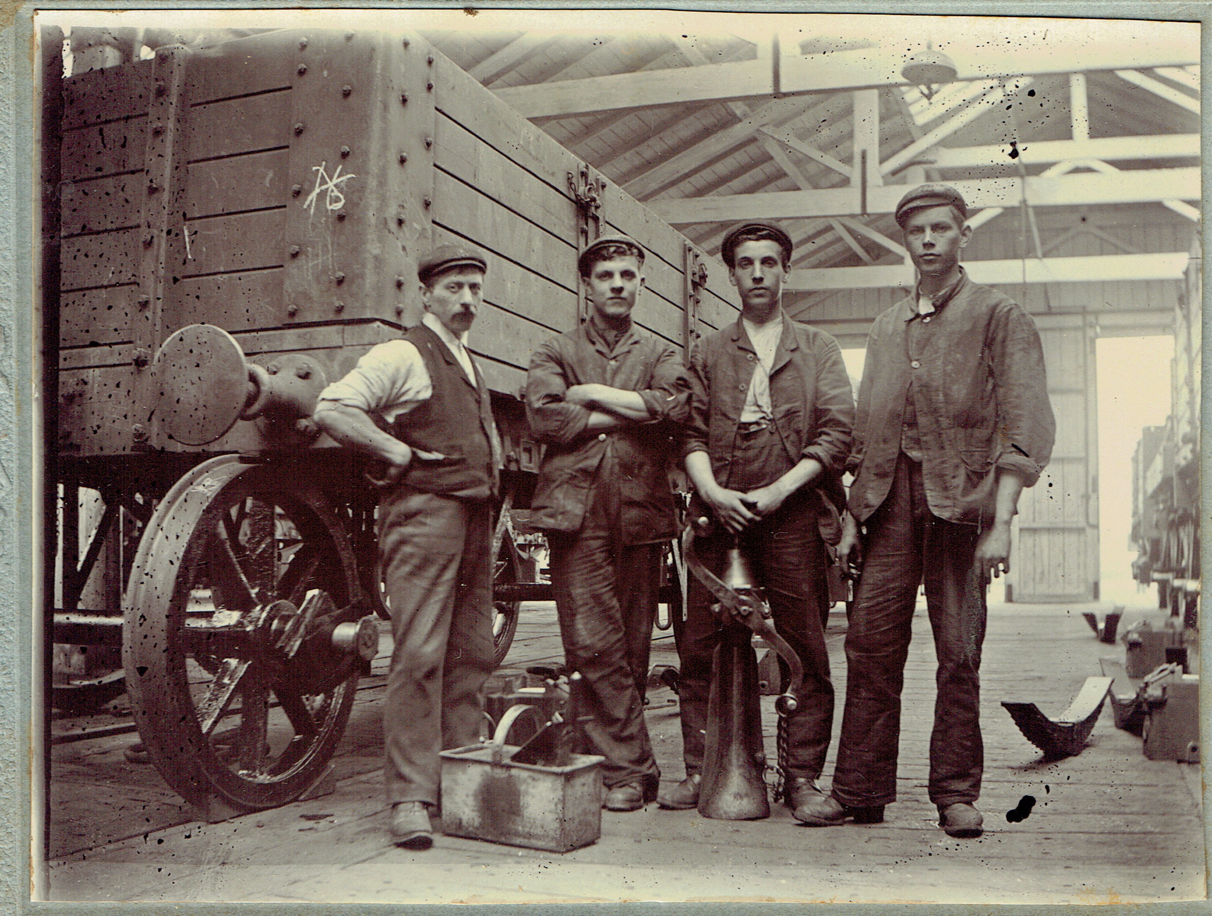 Four men in a wagon repair shop pose in front of a Midland Railway open wagon in the course of repair