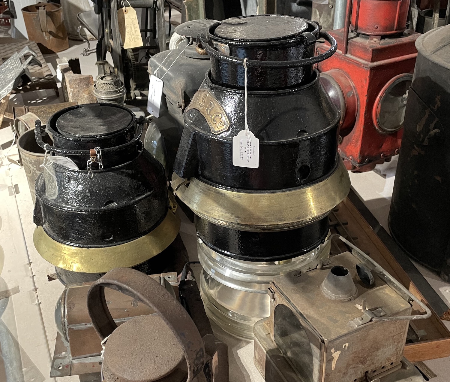 Two large lamps, plainted back with a brass ring at mid-height and glass beneath (though the glass is absent from one of them). A large handle is fixed to the top.