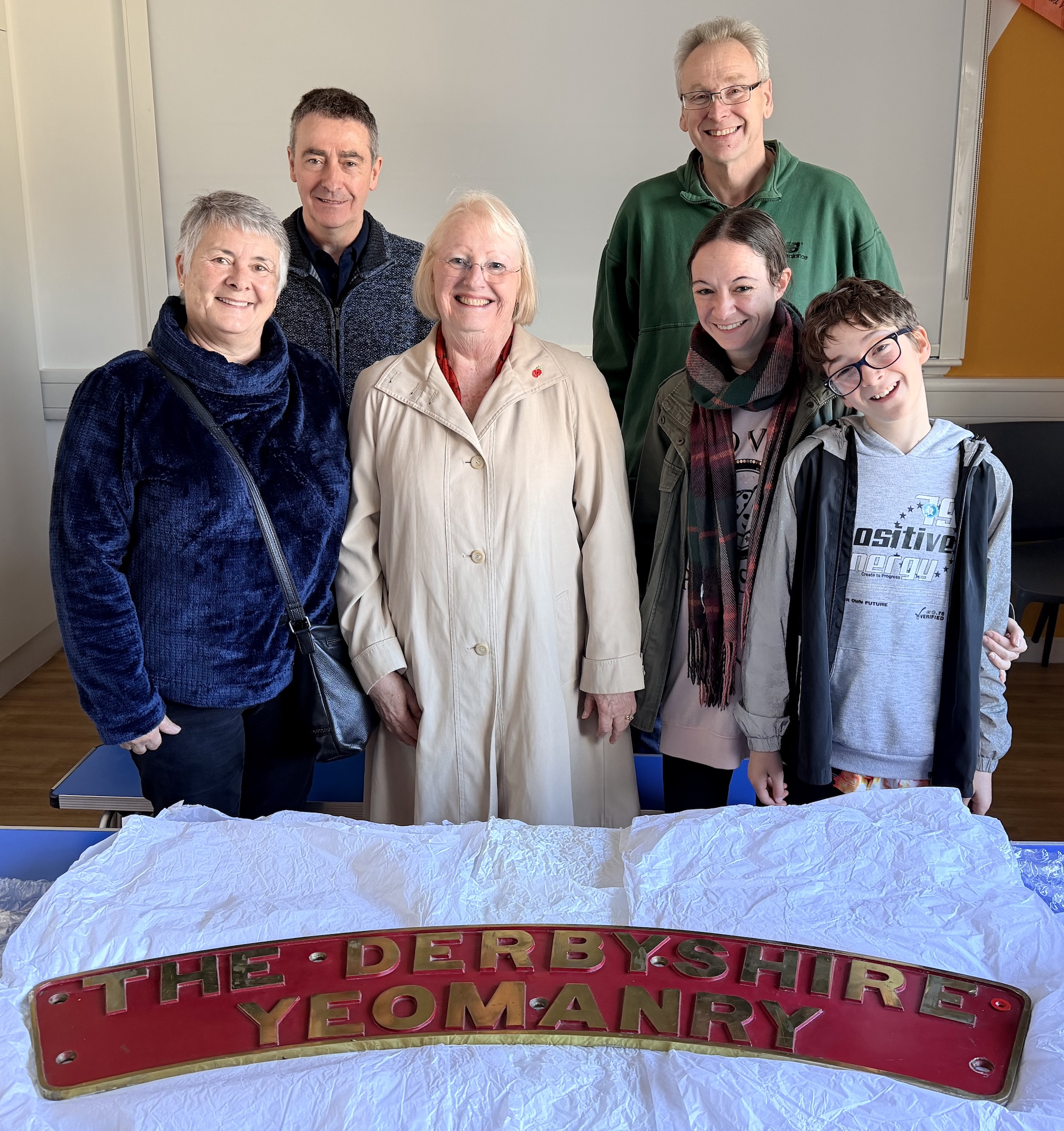 A group of people pose behind the locomotive nameplate The Derbyshire Yeomany laid on a table in front